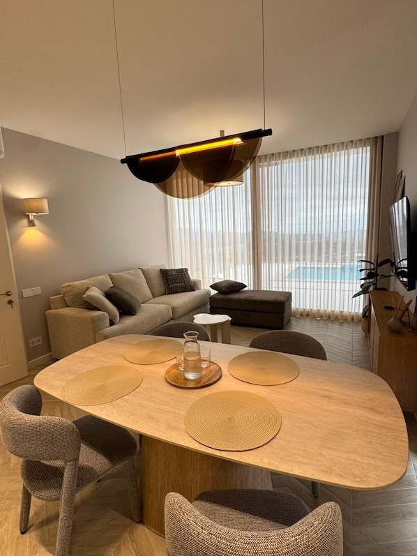 A modern living room with a round dining table, sofas, and a large window with a view.