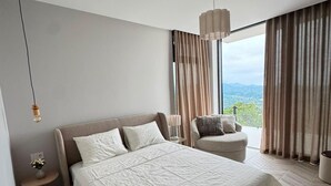 A modern bedroom with a large bed, a bedside table with a lamp, a chair, and a view of the outdoors. - Villa With a Panoramic Bathtub and Pool Overlooking a Beautiful View of Batumi (kapreshumi)