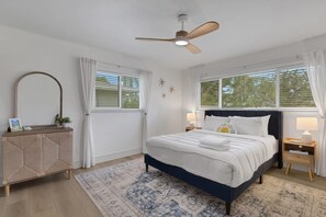 A bedroom with a bed, a ceiling fan, a nightstand, a dresser, and two windows with curtains. - Seacrest Bungalow - Cozy, Family, Beach @ 10 min (Largo)