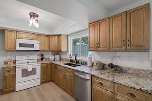A kitchen with wooden cabinets, a white microwave, a double oven, a sink, and a dishwasher. - Seacrest Bungalow - Cozy, Family, Beach @ 10 min (Largo)