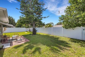 A backyard with a patio area, a large tree, and a white fence. - Seacrest Bungalow - Cozy, Family, Beach @ 10 min (Largo)