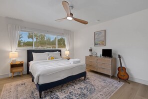 A bedroom with a bed, nightstands, a dresser, a guitar, a ceiling fan, and a window with curtains. - Seacrest Bungalow - Cozy, Family, Beach @ 10 min (Largo)