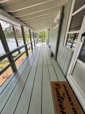 A covered wooden deck with a view of a lake, a doormat, and a door with a window. - Maranacook Lake Cabin: 3BR+detached bunkhouse, Porch,summer Dock on .5 Acre. (Winthrop)