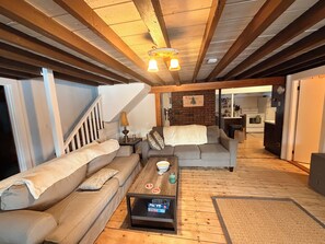 A cozy living room with a wooden ceiling, a sofa, a coffee table, and a staircase leading to another room. - Maranacook Lake Cabin: 3BR+detached bunkhouse, Porch,summer Dock on .5 Acre. (Winthrop)