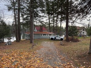 A house with a red roof, a white truck parked in front, and a dock extending into a lake. - Maranacook Lake Cabin: 3BR+detached bunkhouse, Porch,summer Dock on .5 Acre. (Winthrop)