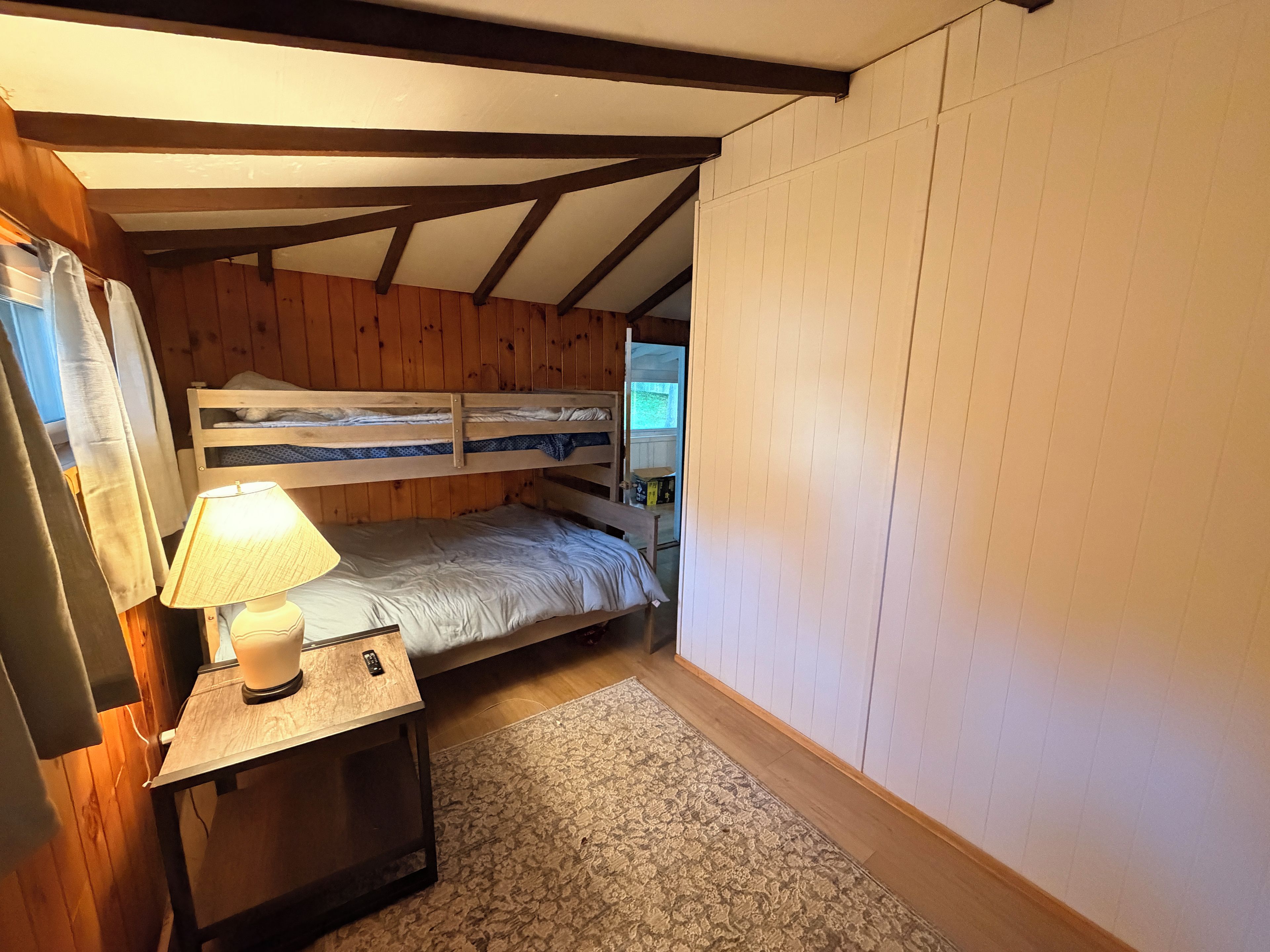 Une petite pièce agréable et chaleureuse, avec un lit superposé, une table de chevet avec une lampe et un tapis à motifs.