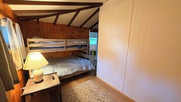 Une petite pièce agréable et chaleureuse, avec un lit superposé, une table de chevet avec une lampe et un tapis à motifs.