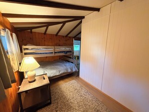 Quarto pequeno e acolhedor com uma cama de solteiro, mesa de cabeceira com luminária e tapete estampado.