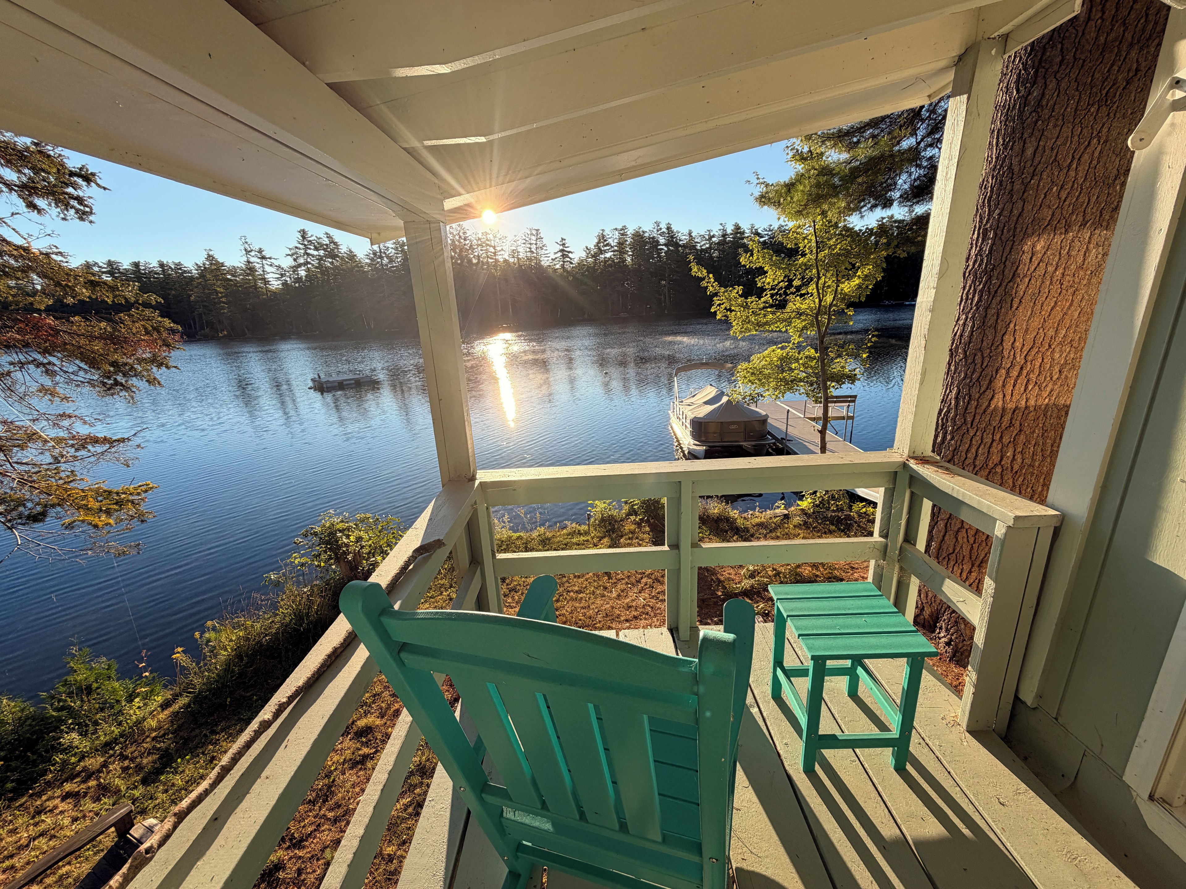 Una terraza de madera con vistas a un lago tranquilo y un muelle con un bote.