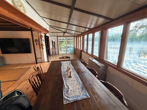 A long dining table with chairs, a rug, and a television on the wall. - Maranacook Lake Cabin: 3BR+detached bunkhouse, Porch,summer Dock on .5 Acre. (Winthrop)