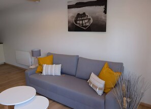 A modern living room with a grey sofa, a white round table, and a painting of a boat on water. - Apartment 'Au Martin Pêcheur Côté Rivière' with Wi-Fi (Plobsheim)