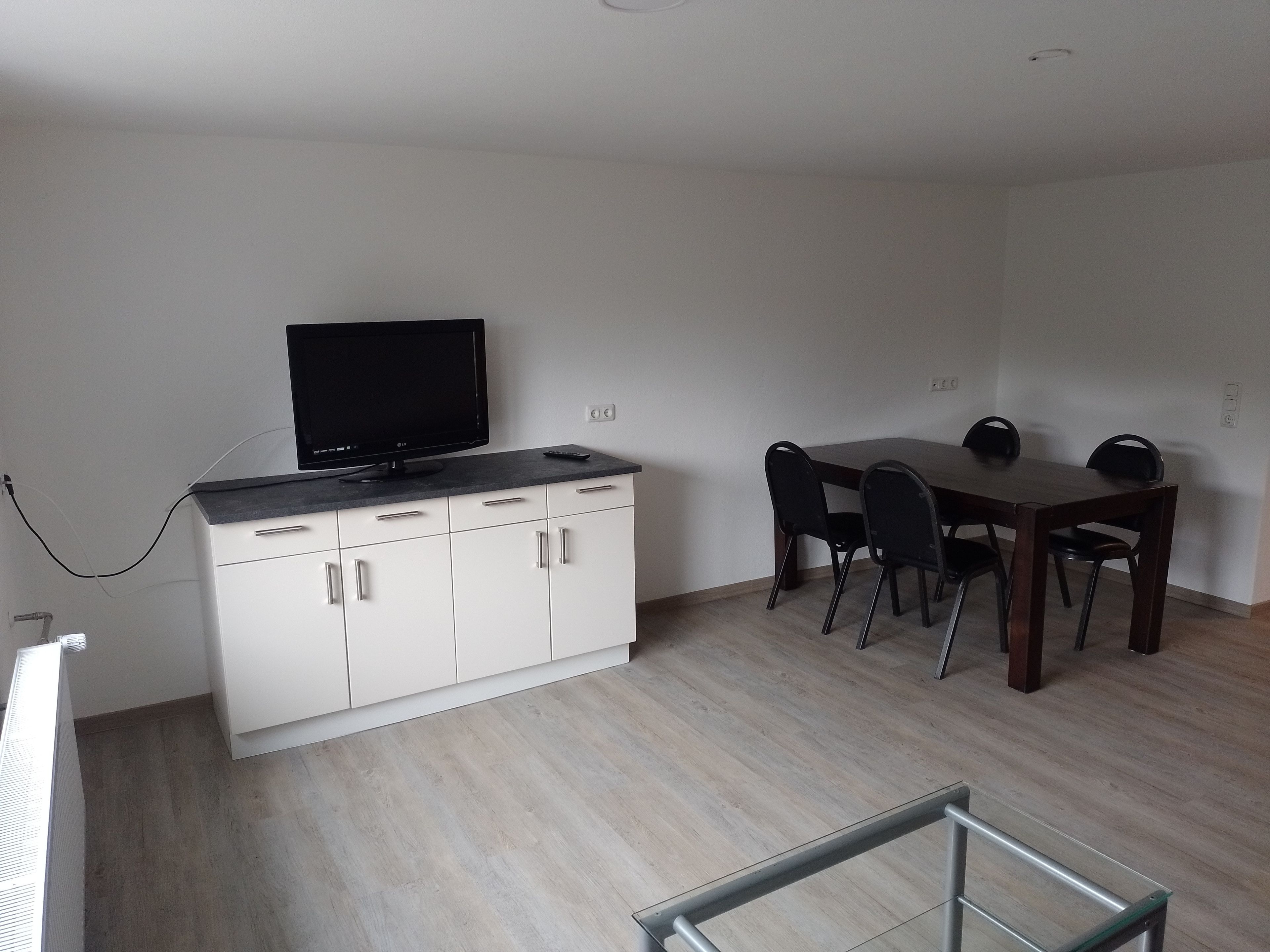 Une pièce comprenant une table à manger, des chaises, un téléviseur posé sur un meuble et un radiateur.