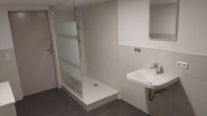 Un baño con cabina de ducha de vidrio, un lavamanos blanco y un espejo sobre él.