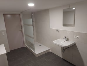 Casa de banho com cabine de chuveiro em vidro, lavatório branco e espelho em cima.