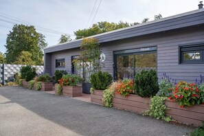 A modern building with a grey exterior, large windows, and a variety of plants and flowers in front.