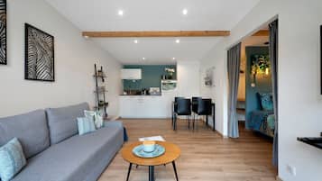 Ein modernes Wohnzimmer mit einem grauen Sofa, einem Holztisch und einer Küche im Hintergrund.