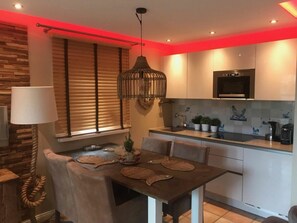 A modern kitchen with a dining area, featuring a table with placemats, a hanging light fixture, and a window with blinds. - Apartment in Westerland With Swimming Pool (Sylt)