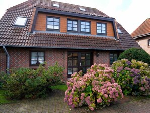 Ein zweistöckiges Haus mit einem Ziegeldach, Backsteinwänden und einer Haustür. Im oberen Stock befinden sich zwei Fenster und ein kleines Dachfenster.