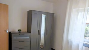 Un dormitorio con cama, armario, puerta y ventana con cortinas.