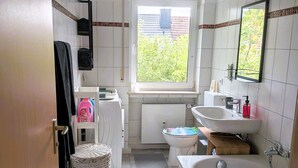 Un baño con bañera, inodoro, lavamanos y ventana con vistas a la vegetación exterior.