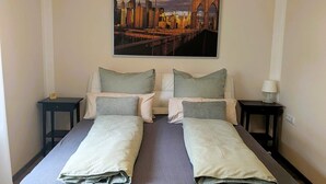 Una cama doble con un cuadro de un paisaje urbano en la pared superior, dos mesitas de noche y un reloj.