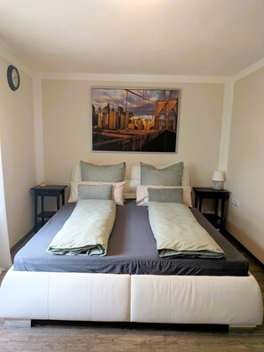 En dubbelsäng med en tavla som föreställer en stadsbild ovanför, två sängbord och en klocka på väggen.