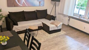 Una sala de estar con un sofá, una mesa de comedor con sillas, una lámpara de pie y un cuadro grande en la pared.