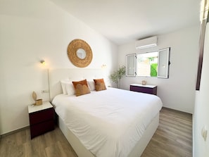 Ein Schlafzimmer mit einem großen Bett, einem Nachttisch, einem Wandspiegel und einem Fenster mit Blick.