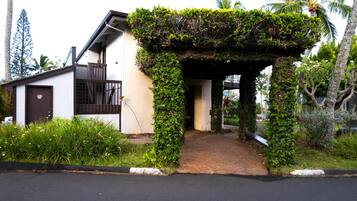 A house with a covered entrance, a small porch, and a garden with various plants and a palm tree.