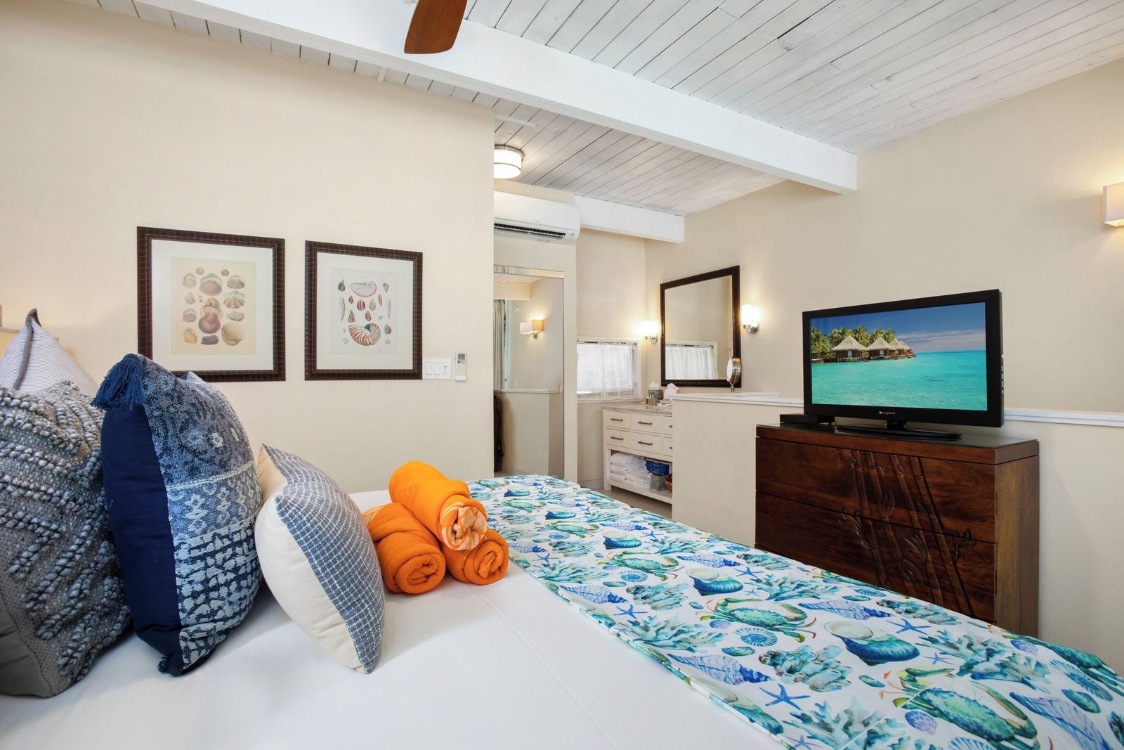 Una habitación de hotel con una cama, televisión, cómoda y obras de arte enmarcadas en la pared.