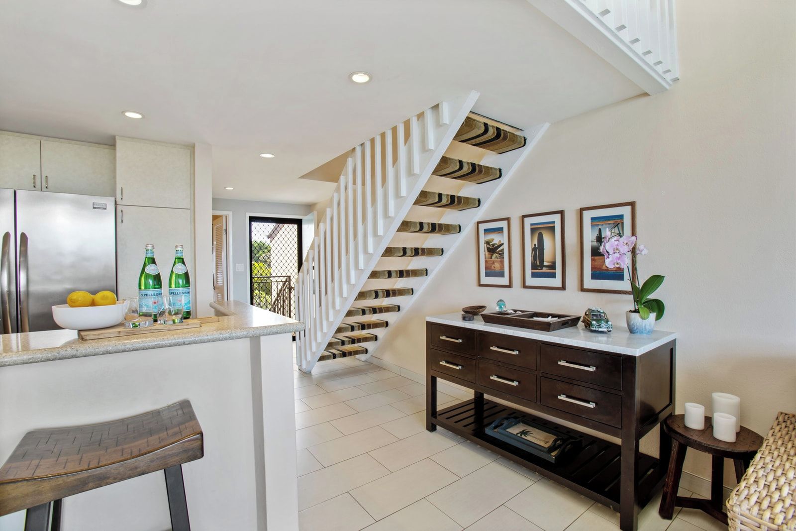 A modern kitchen with a central island, a staircase with a unique design, and a dining area with a bar stool.