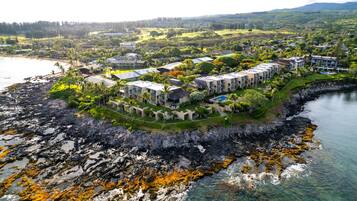 An aerial view of a coastal resort with multiple buildings, a rocky shoreline, and clear waters.