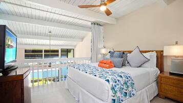 A hotel room with a bed, a TV, a ceiling fan, and a view of the ocean.