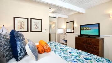 A hotel room with a bed, pillows, a dresser, a television, and framed artwork on the wall.