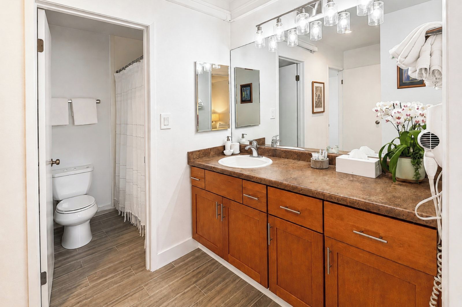 Un baño con inodoro blanco, tocador de madera y un espejo grande.