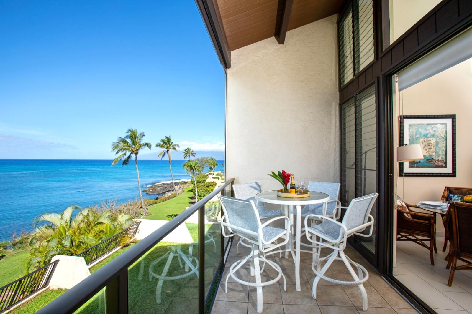 Un balcon avec une table et des chaises, une vue sur l’océan et un tableau encadré au mur.