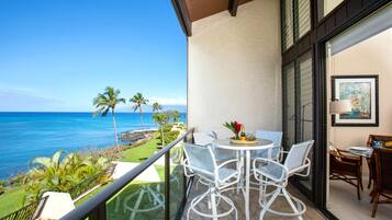 Un balcon avec une table et des chaises, une vue sur l’océan et un tableau encadré au mur.