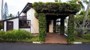 A house with a covered entrance, a small porch, and a garden with tropical plants.