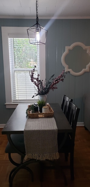 A dining area with a table set for two, a hanging light fixture, a window with blinds, and a decorative wall piece. - Three Rivers Retreat (Lake City)