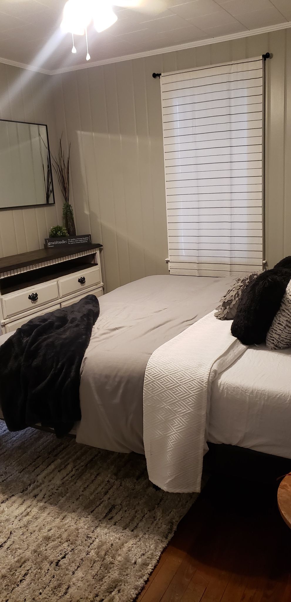 Ein Schlafzimmer mit einem Bett, Nachttischen, einer Kommode, einem Teppich und einem Fenster mit Jalousien.