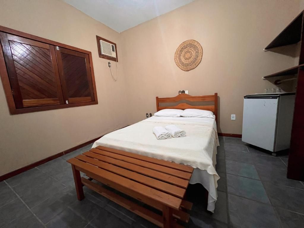 Un dormitorio con cama, un banco de madera, un refrigerador pequeño y un equipo de aire acondicionado instalado en la pared.