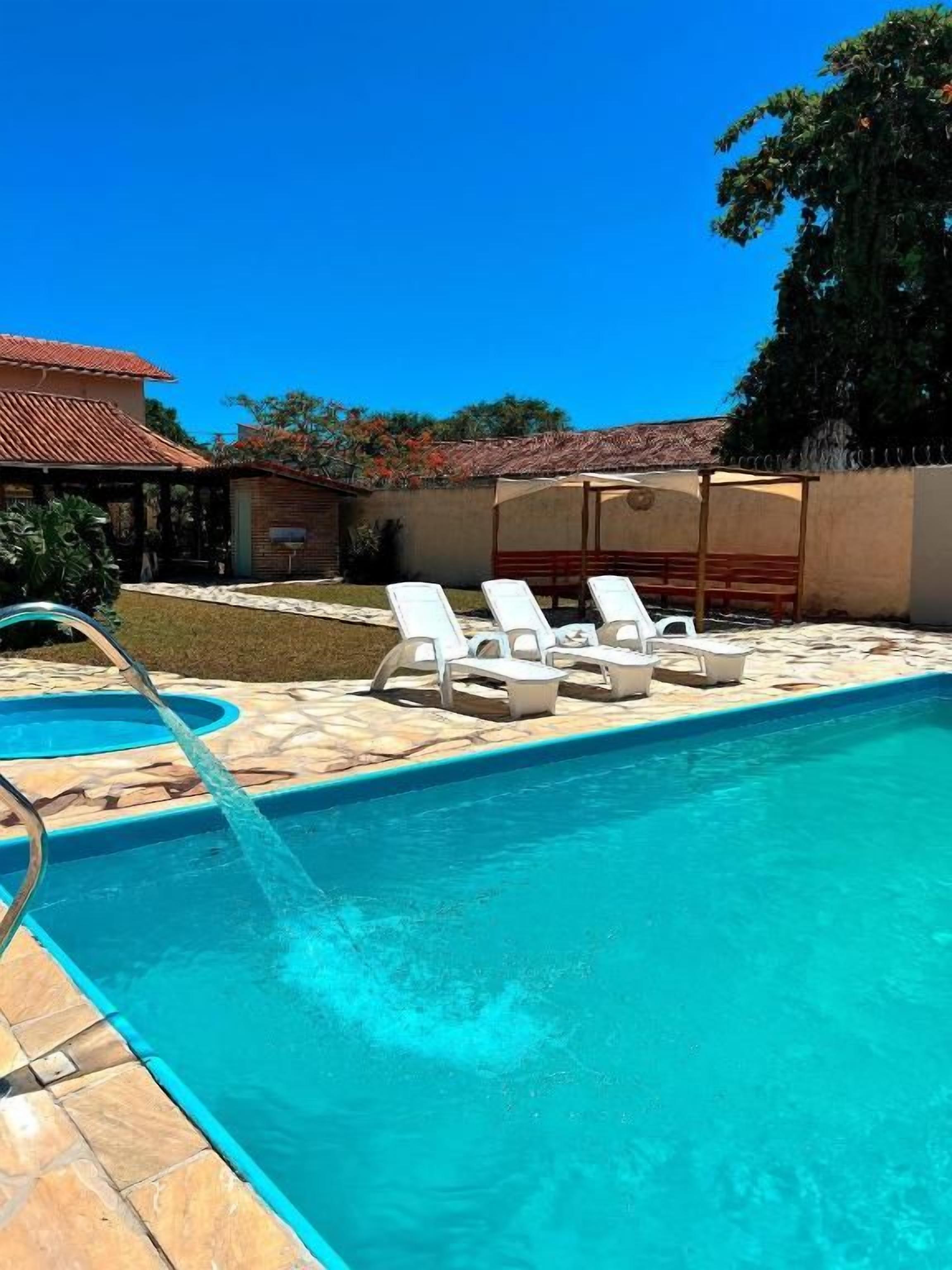 A swimming pool with a water feature, surrounded by lounge chairs and a covered area.