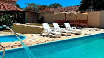 A swimming pool with a water feature, surrounded by lounge chairs and a covered area.