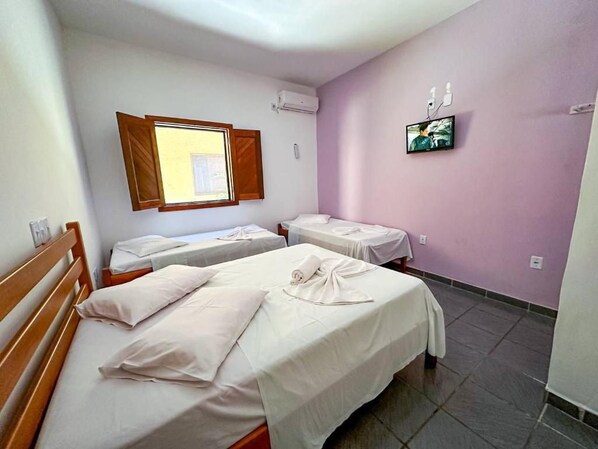 A hotel room with two beds, a television, and a window with blinds.