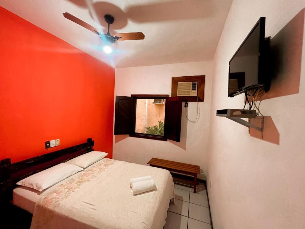 A bedroom with a bed, a ceiling fan, a TV mounted on the wall, and a window with an air conditioning unit.