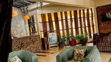Un hall con mobiliario de mimbre, una recepción y plantas en macetas.