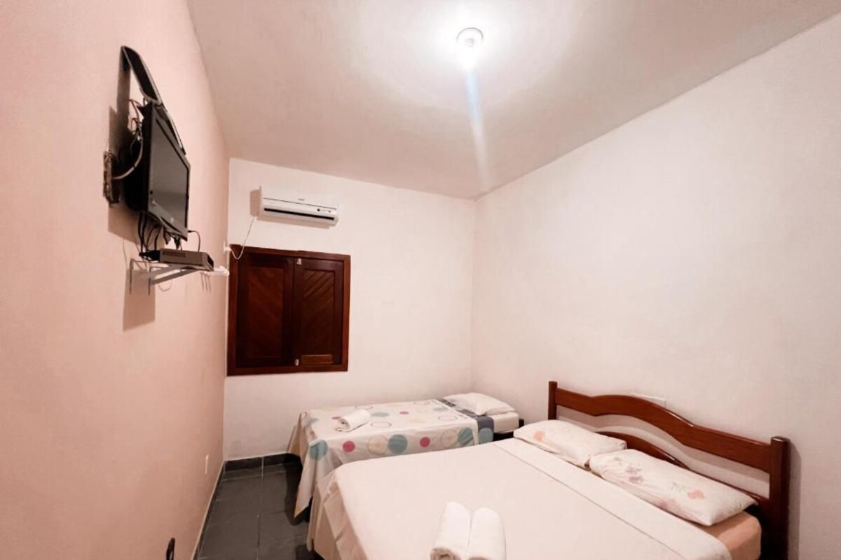 A small hotel room with two beds, a television, an air conditioning unit, and a wooden door.