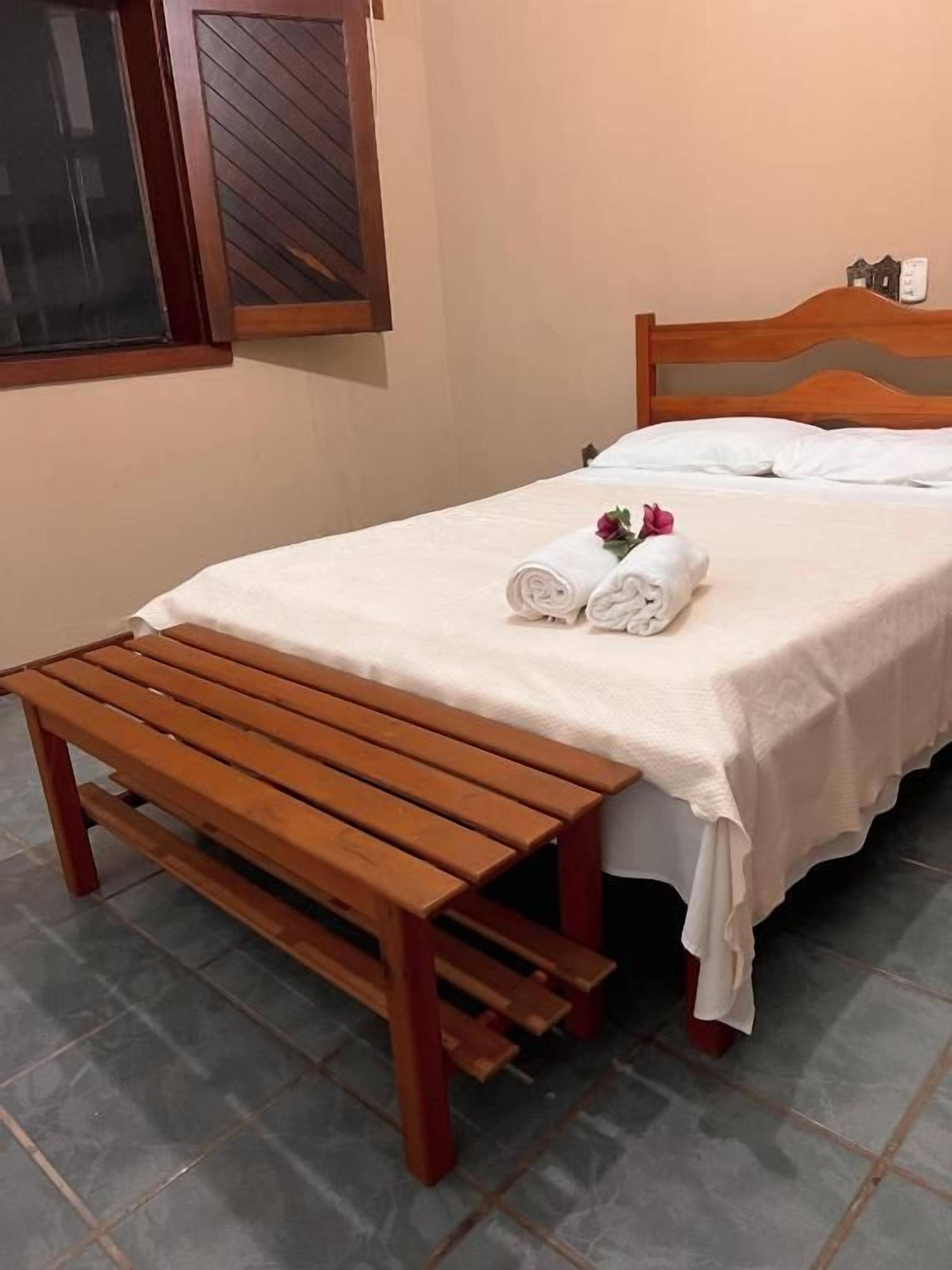 Een slaapkamer met een bed, een houten bankje en een raam.
