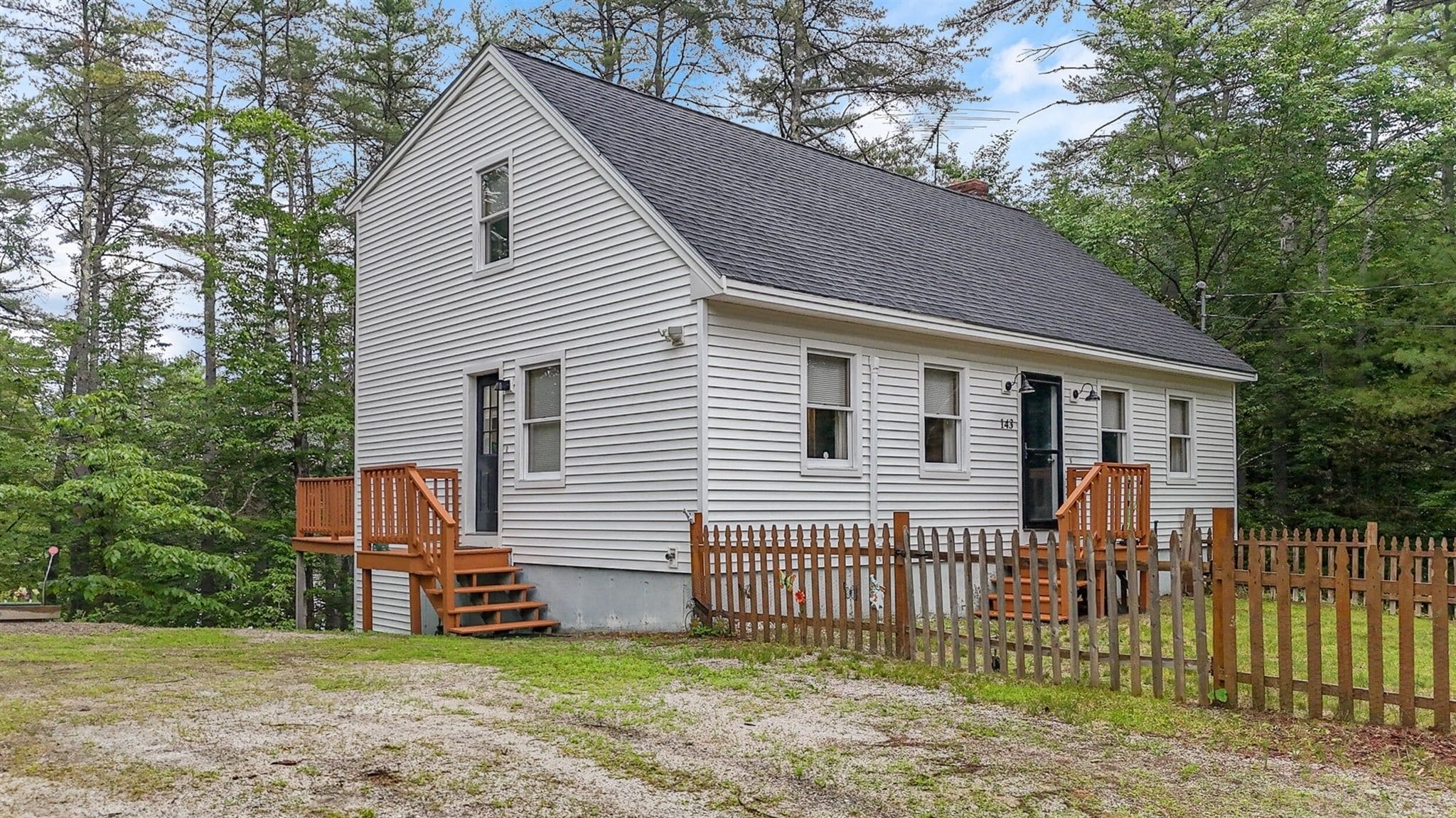 A single-story house with a gabled roof, a front porch with a wooden railing, and a picket fence.