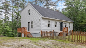 Une maison de plain-pied avec un toit à pignon, une véranda à l’avant avec une balustrade en bois et une clôture à piquets.